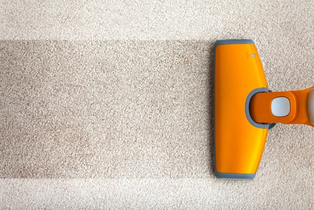 Orange vacuum cleaner cleaning beige carpet