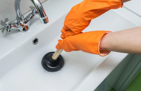 person unclogging sink drain while wearing bright orange rubber globes
