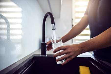 Person filling up glass of water from modern sink tap in new kitchen