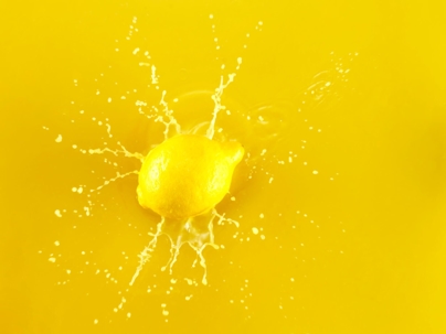 A bright, fresh, yellow lemon splashing against a bright yellow background