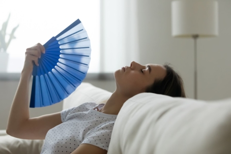 woman trying to cool down with fan on couch