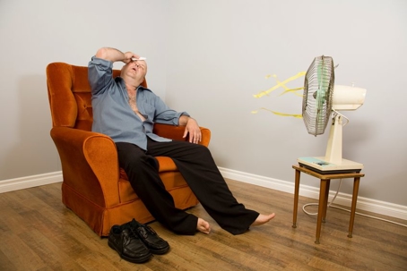 uncomfortable man sitting in front of fan